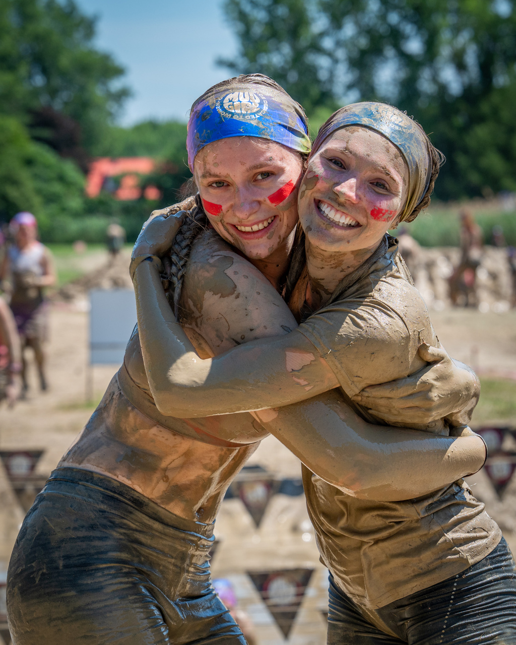 Two smiling, mud-covered participants embrace during an outdoor event.