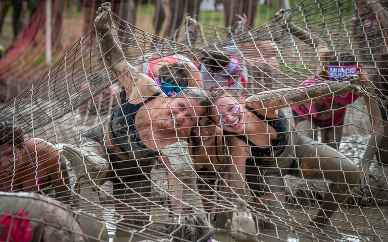 A participant crawls beneath a low rope net surrounded by other racers.