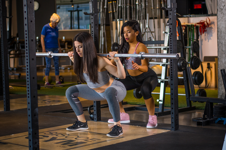 Two athletes practise barbell squats together in a gym.