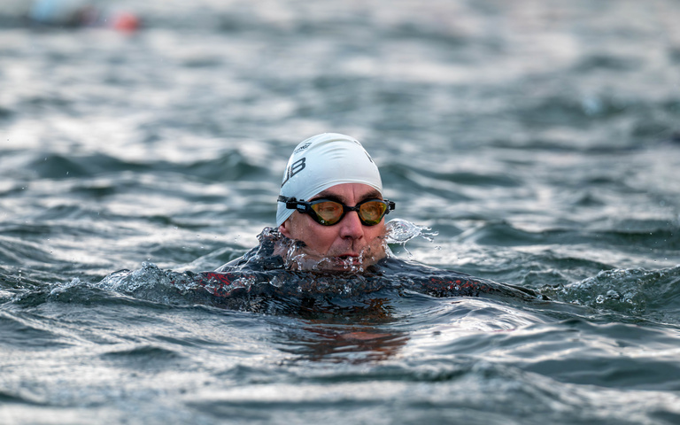 A swimmer wearing a white cap and goggles moves through open water.
