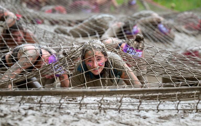 Participants crawl through muddy water beneath a low rope net.