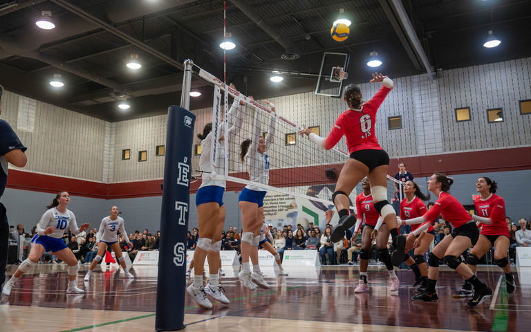 Volleyball players jump at the net as teammates watch the ball.