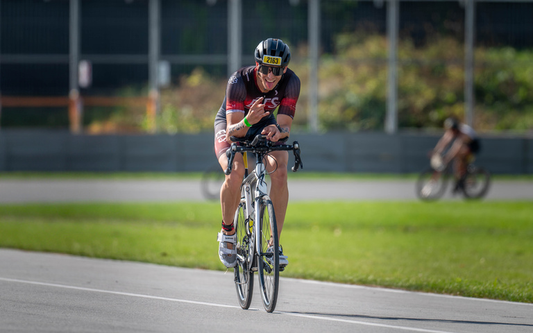 A cyclist leans over the handlebars while riding on the road.