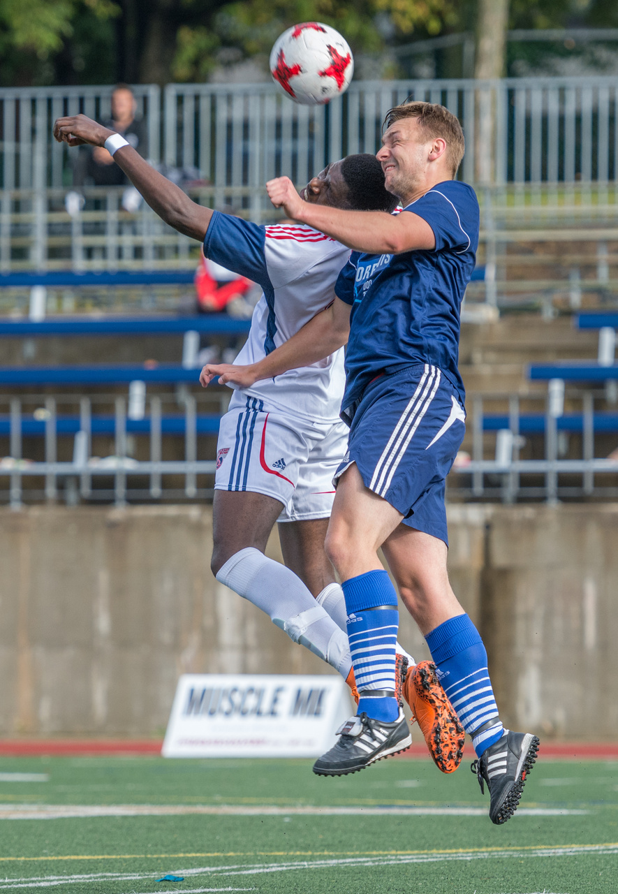 Two soccer players jump to contest the ball in midair.
