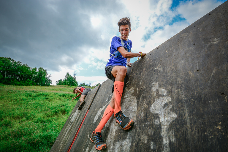 A young participant in a blue shirt climbs over a tall outdoor wall.