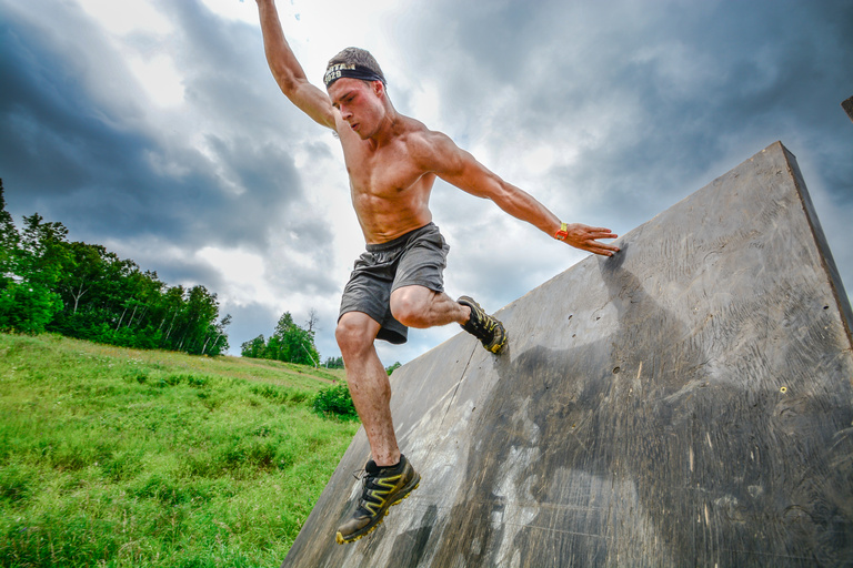 A racer balances with one hand on an obstacle wall while stepping down.