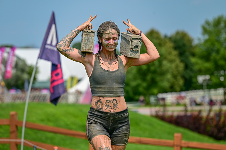 A mud-covered participant raises both hands with a smile on the course.